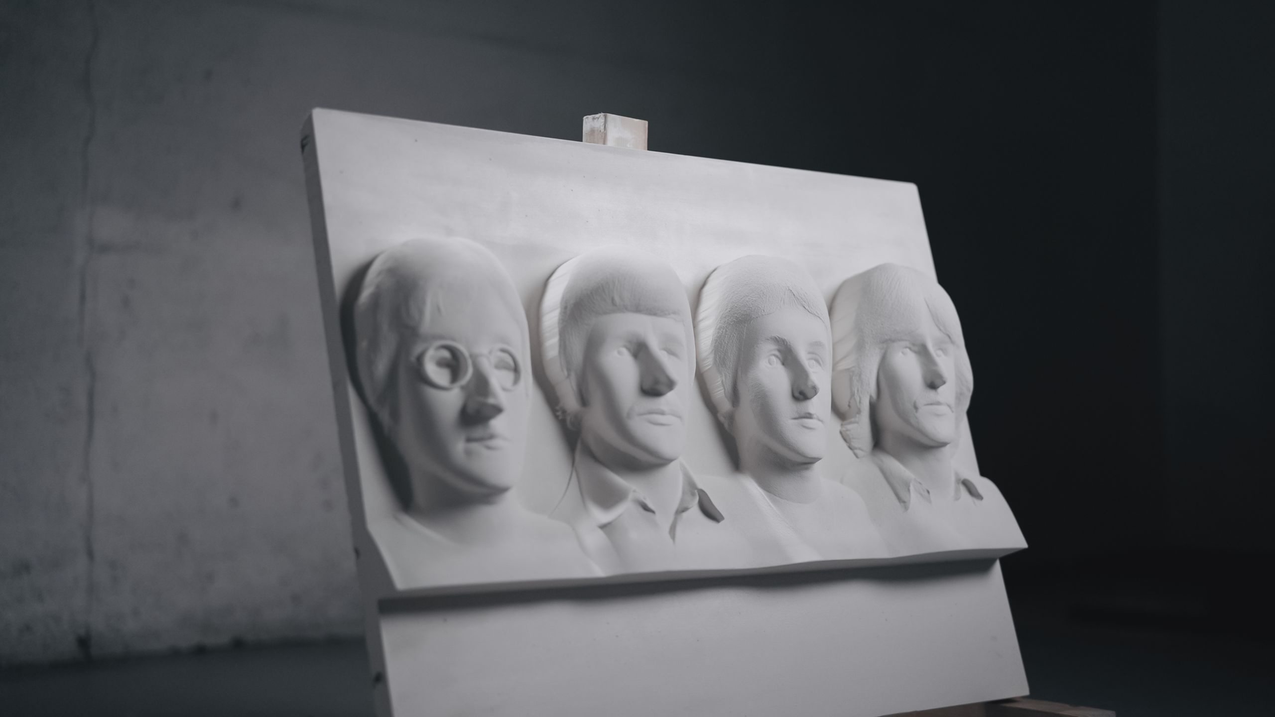 The four members of the Beatles as they appeared in 1967 are carved into plaster. The artwork sits on a stand in an empty workshop